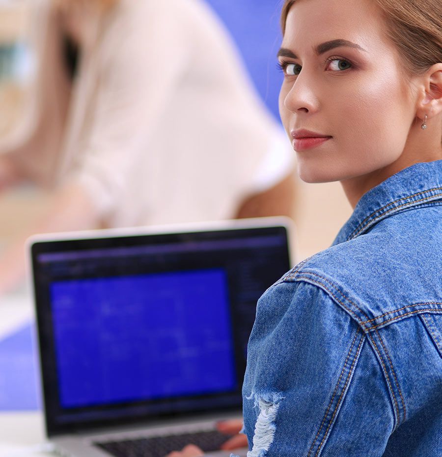 Una mujer con una chaqueta vaquera está sentada frente a una computadora portátil.