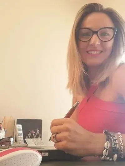 Una mujer con gafas está sentada en un escritorio sosteniendo un bolígrafo.