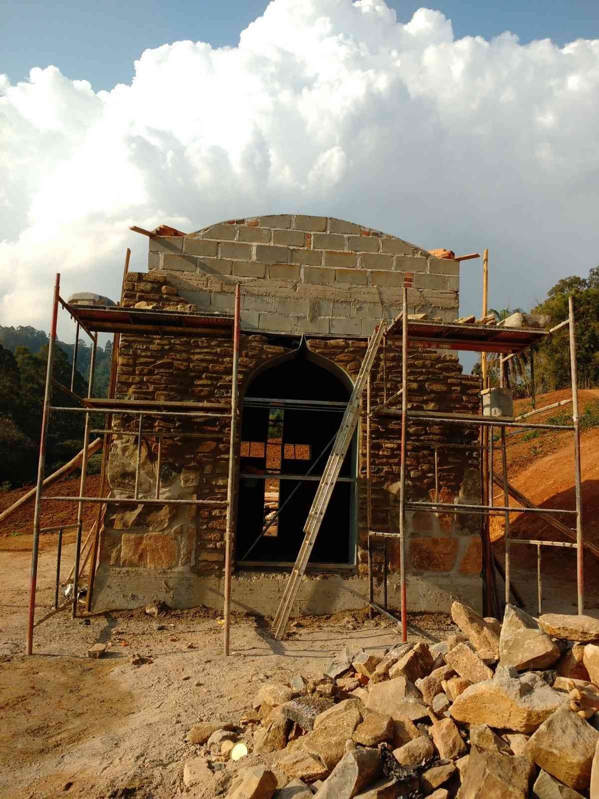 Edificio de piedra en construcción con andamios, puerta arqueada y montones de escombros en la fachada.