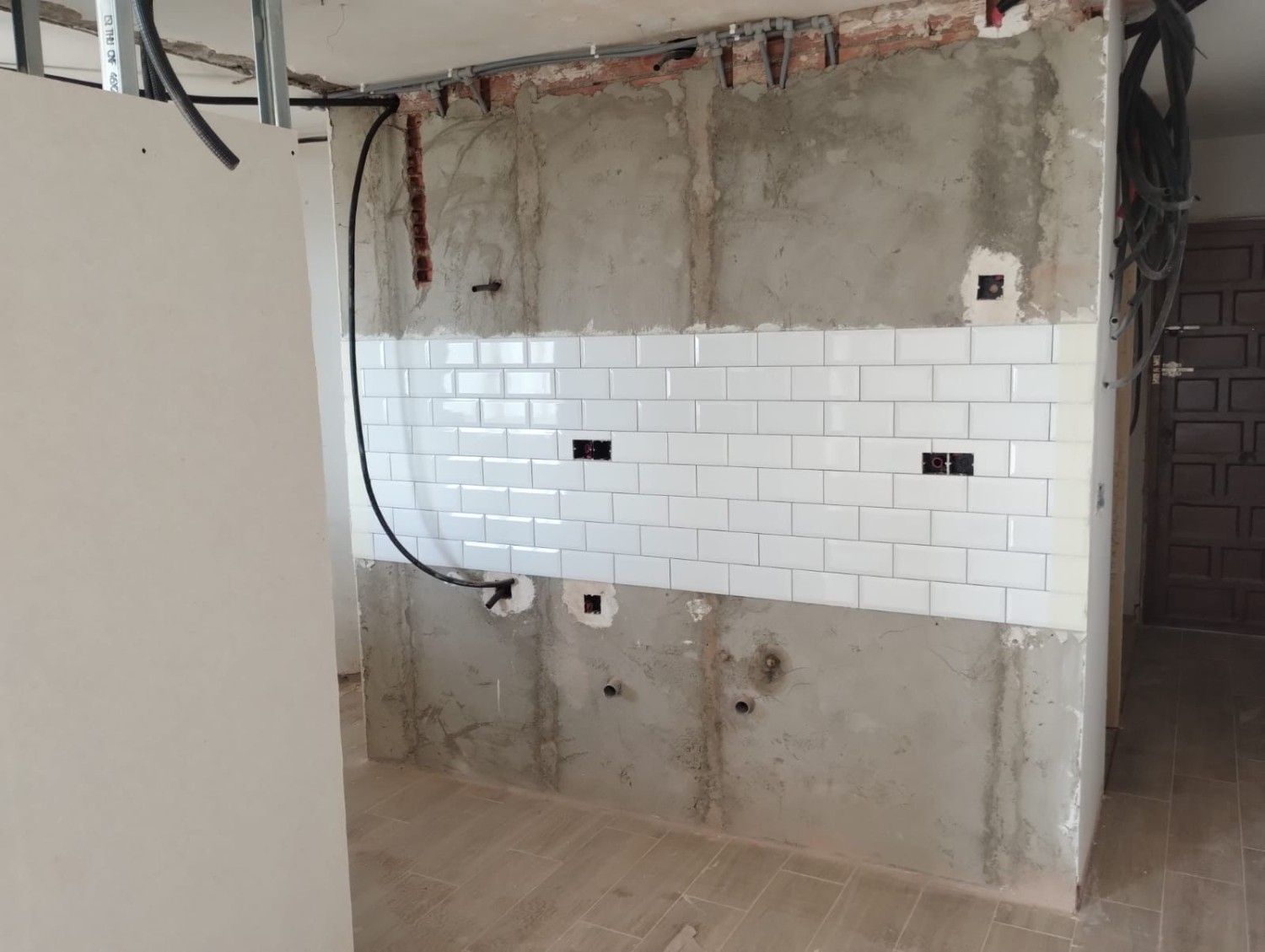 Pared parcialmente alicatada con hormigón visto, cableado y obras de reforma sin terminar.