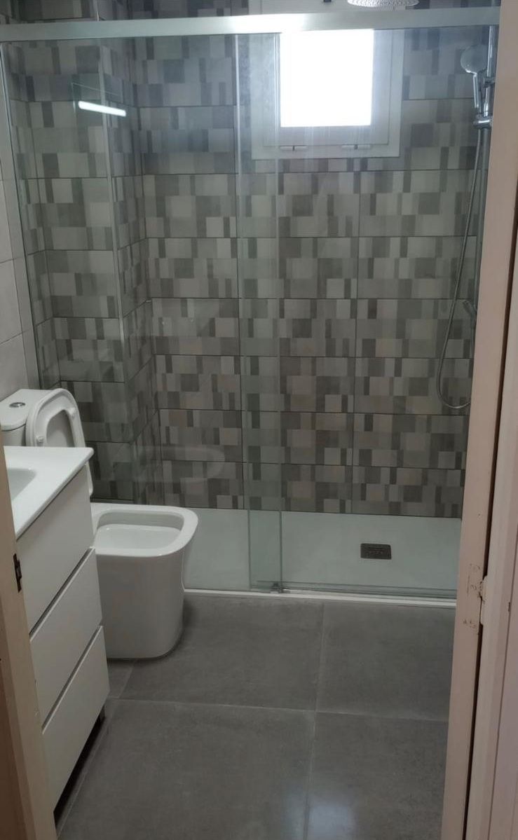 Baño pequeño con inodoro, lavabo, pared de ducha alicatada y ventana esmerilada.