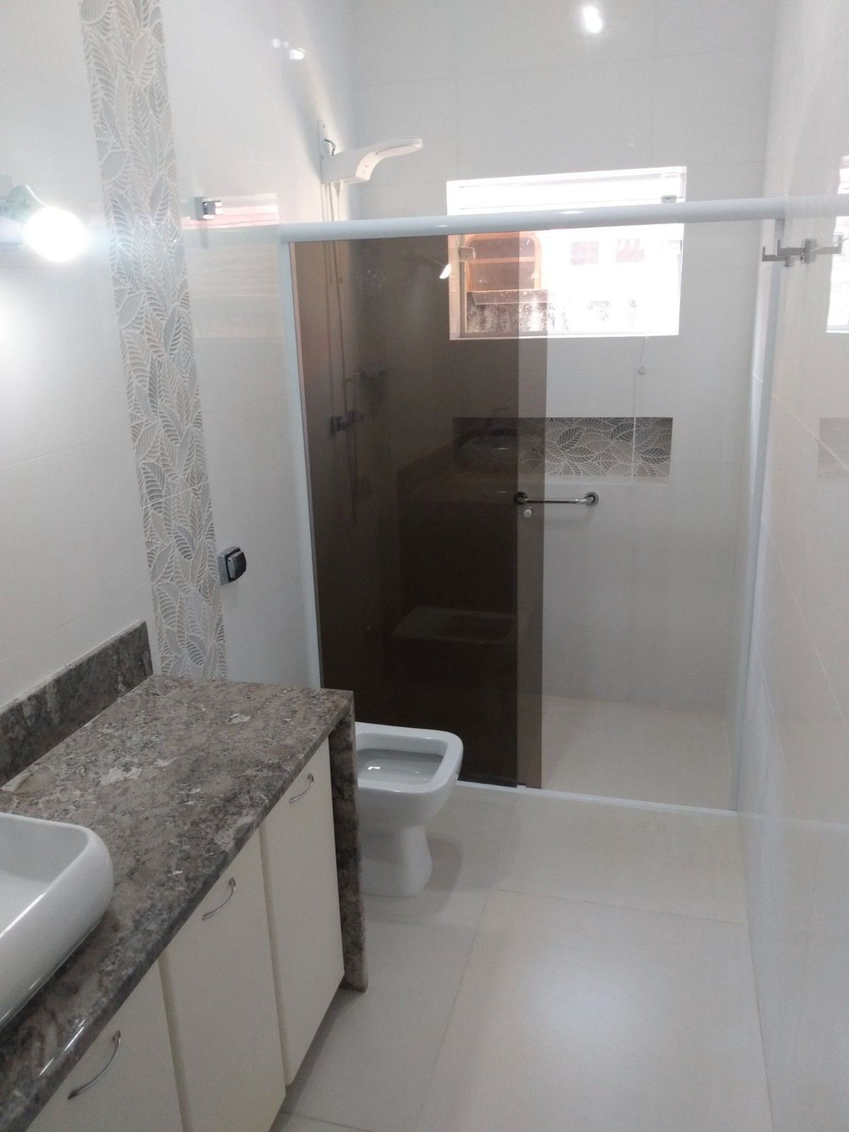 Baño moderno con tocador de granito, espejo de pared, cabina de ducha de cristal, inodoro y azulejos blancos brillantes.