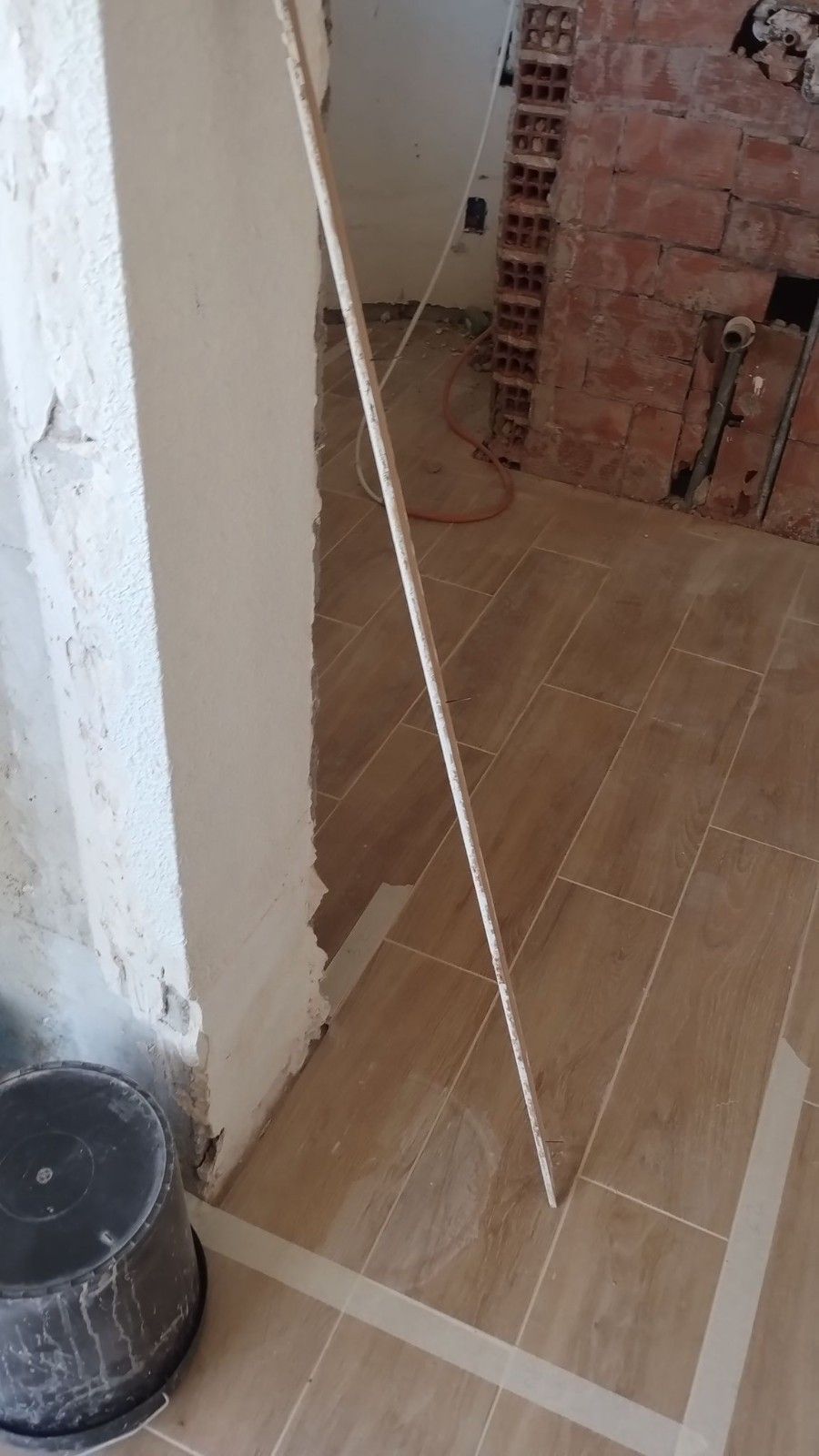 Pasillo interior alicatado con un poste blanco inclinado, pared de ladrillo visto y un cubo negro en la esquina.