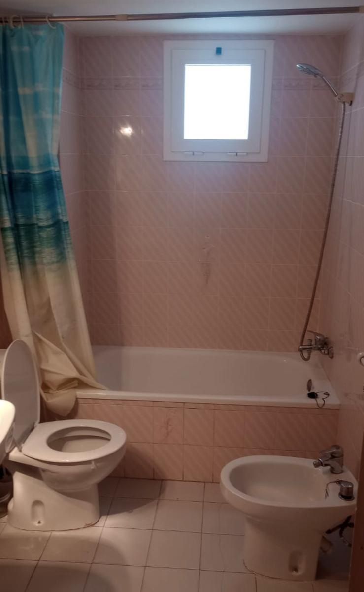 Baño pequeño con bañera/ducha, inodoro, bidé y una ventana encima de la bañera.