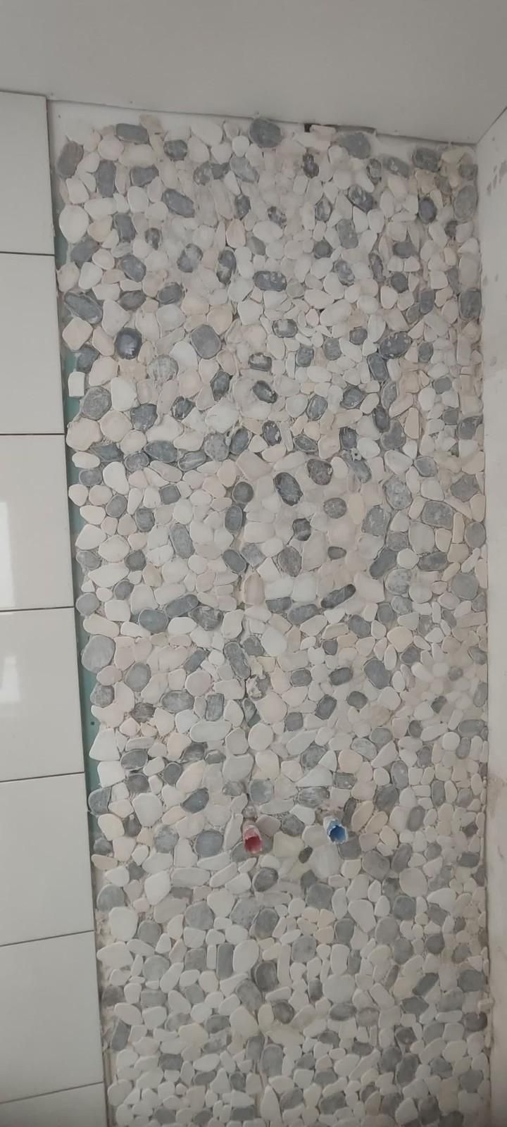 Papel pintado o cortina con estampado floral colgando junto a una pared de azulejos blancos y bordes de armarios.