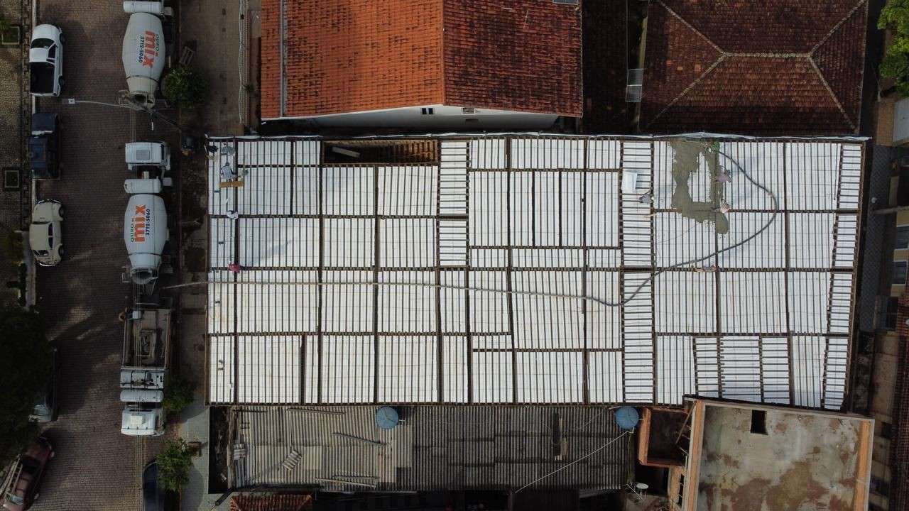 Vista aérea de un edificio con techo de metal blanco, rodeado de coches aparcados y estructuras de ladrillo.