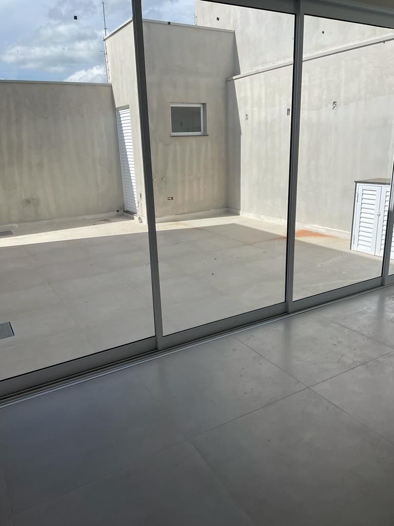 Un patio exterior vacío con paredes de hormigón, puertas de cristal y una pequeña ventana en un día soleado.