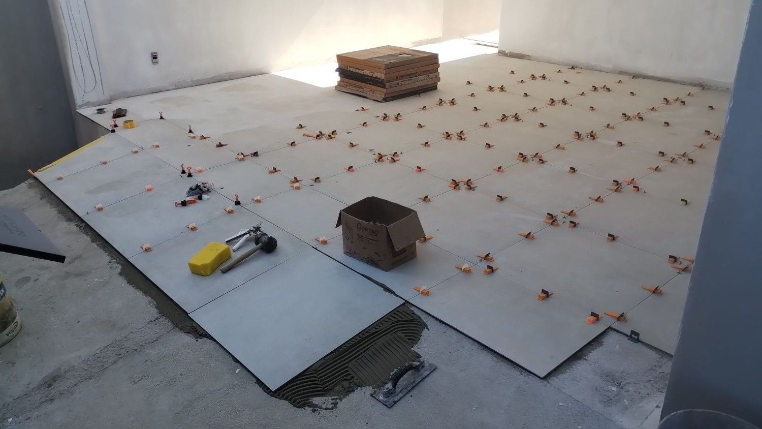 Terraza en construcción con paneles aislantes, marcadores naranjas, ladrillos y una herramienta en el suelo.