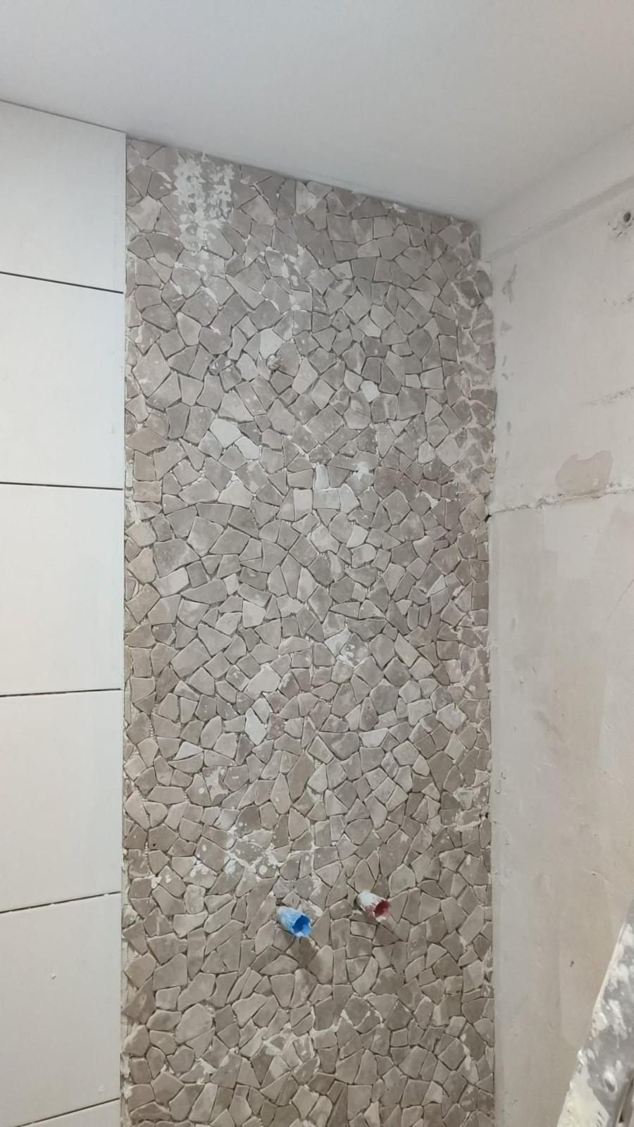 Pared del baño con azulejos grises estampados y conexiones de fontanería a la vista.