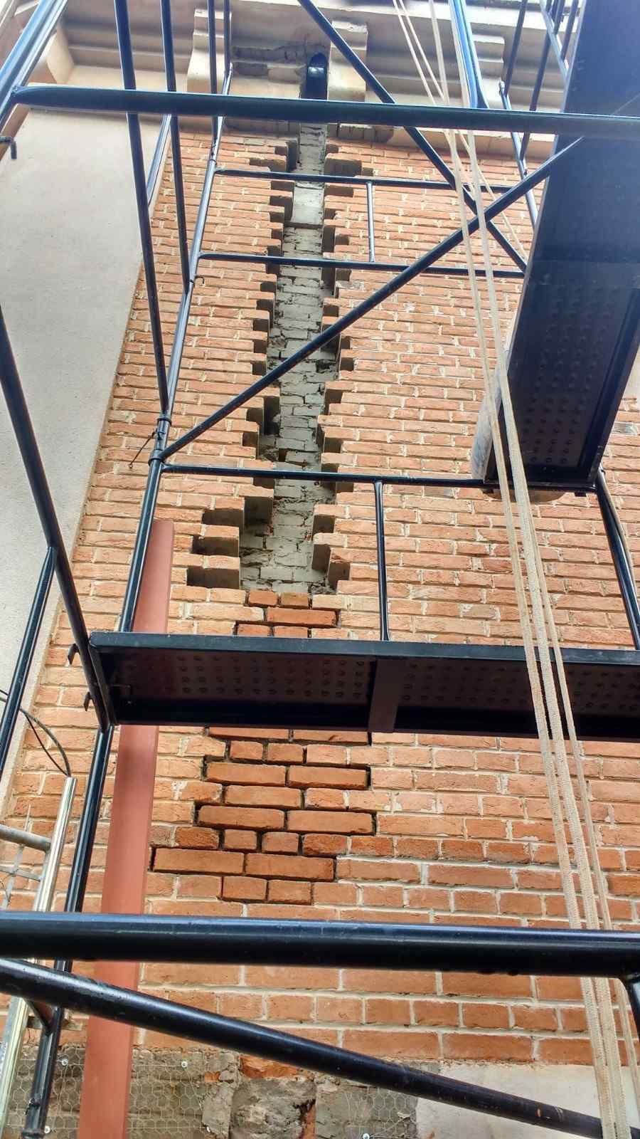 Andamio adosado a una pared de ladrillos con una franja vertical de ladrillos reparados a la vista.