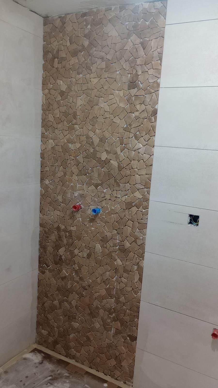 Pared del baño con un panel decorativo de mosaico marrón, laterales alicatados en blanco y tomas de agua.