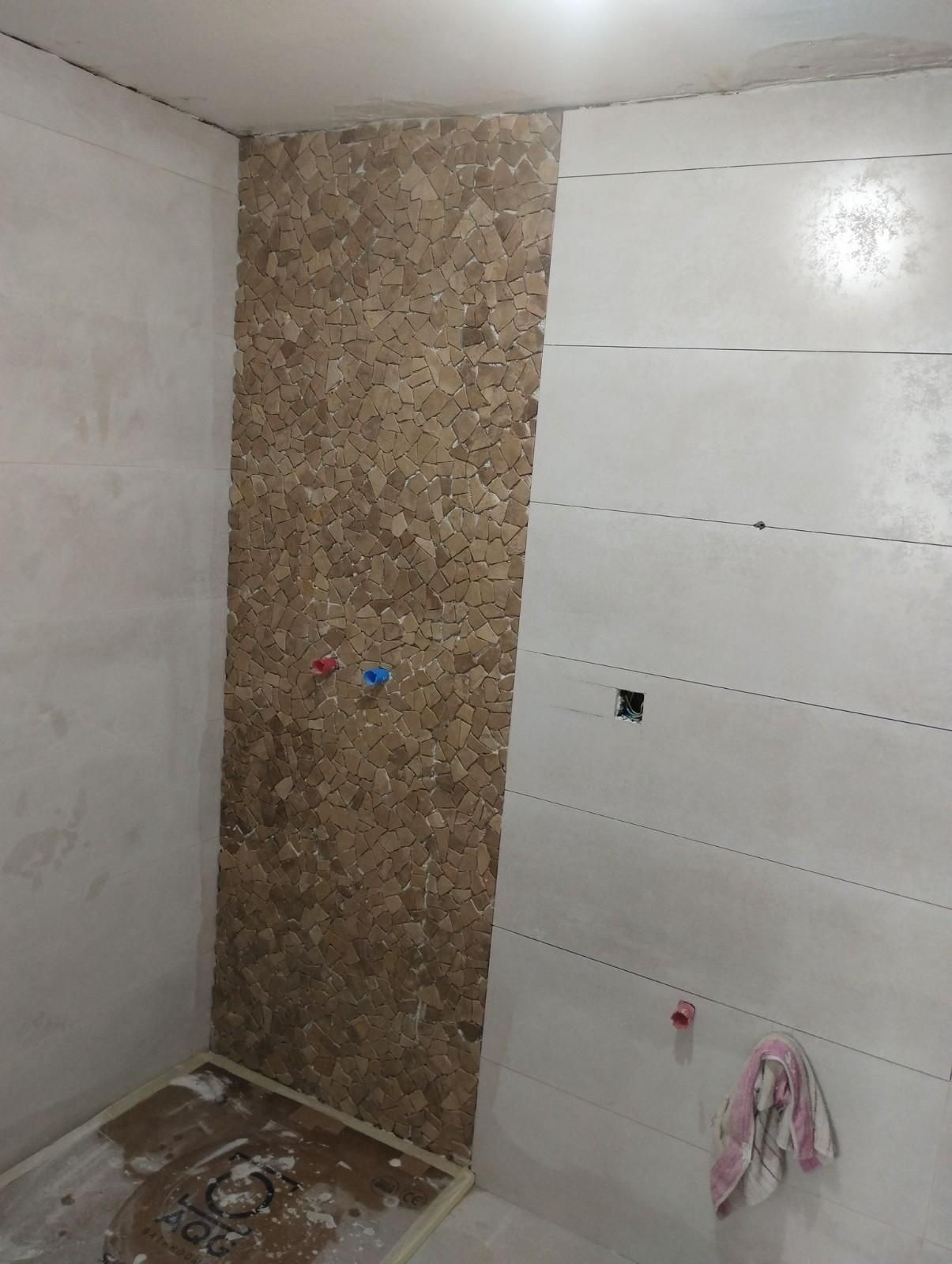 Pared del baño parcialmente alicatada con una estrecha franja decorativa que imita la piedra y grifería a la vista.