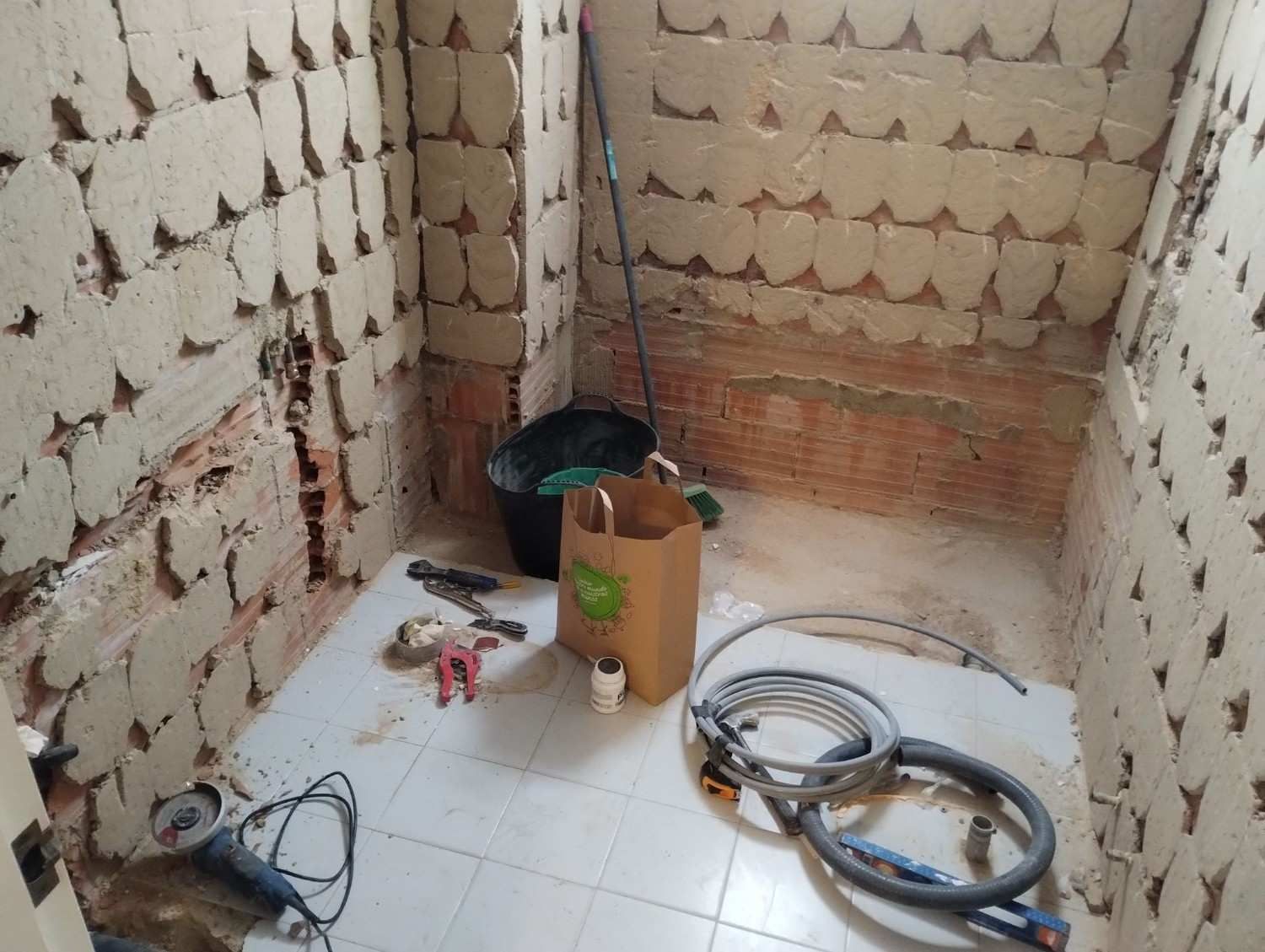 Habitación parcialmente alicatada en obras, con herramientas, cables y cubos en el suelo.