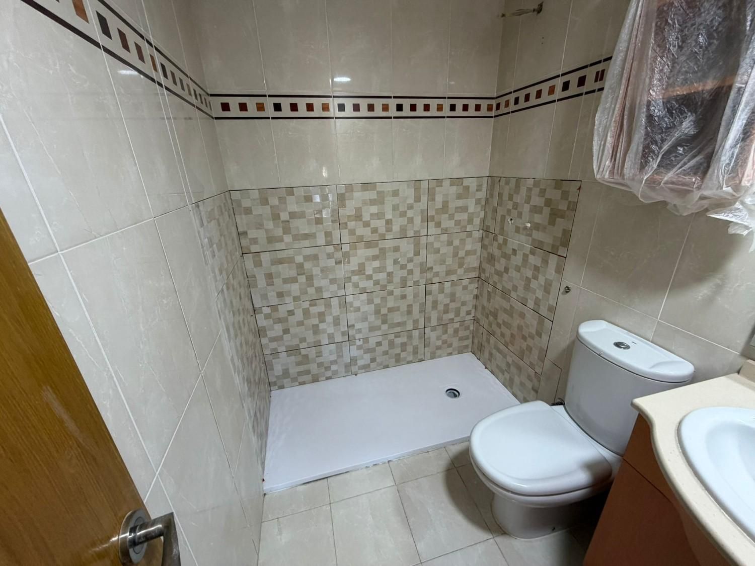 Baño pequeño con azulejos, inodoro, lavabo y plato de ducha blanco.