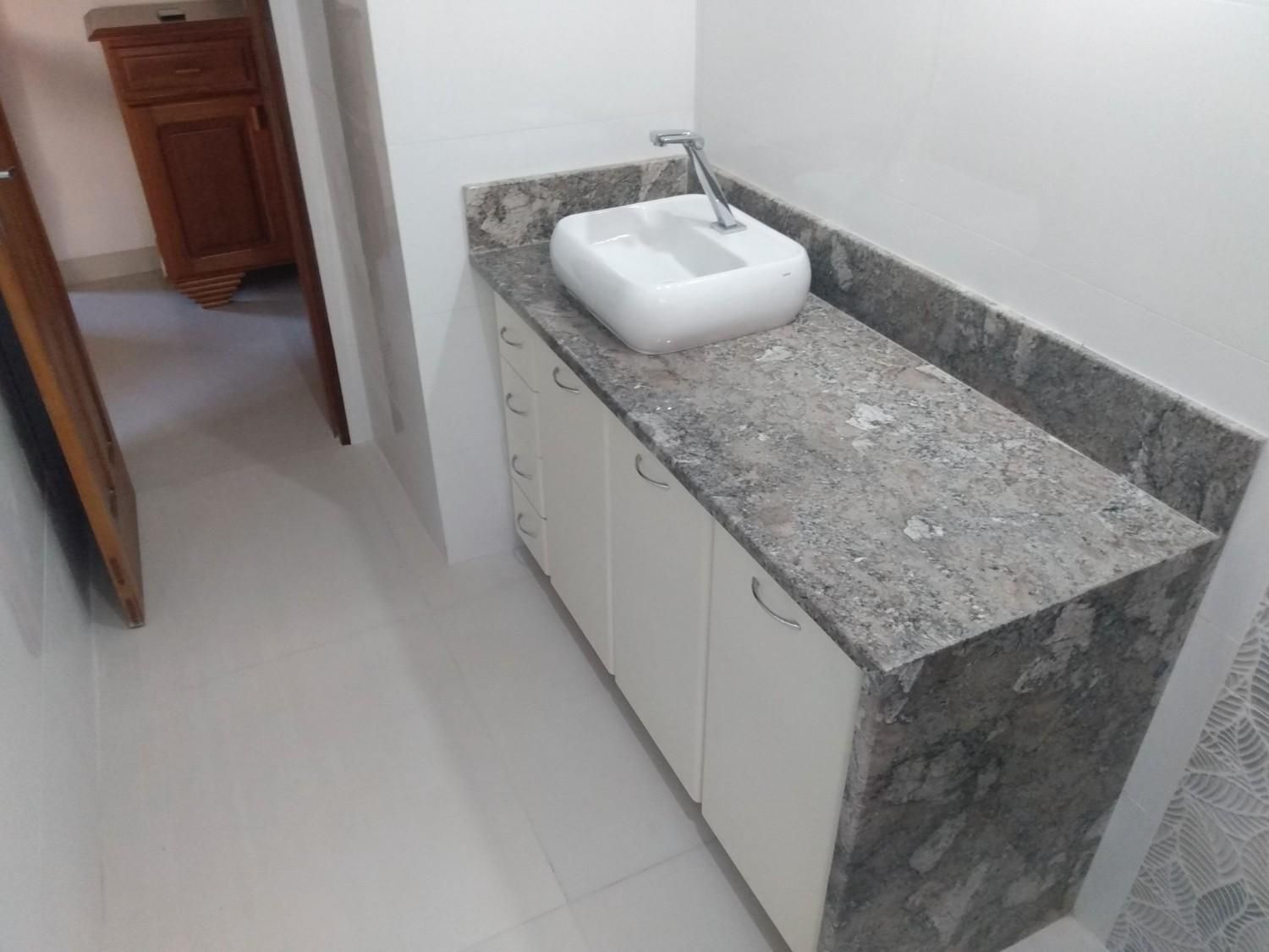 Mueble de baño con lavabo blanco, encimera de granito y puertas de armario contra una pared alicatada.