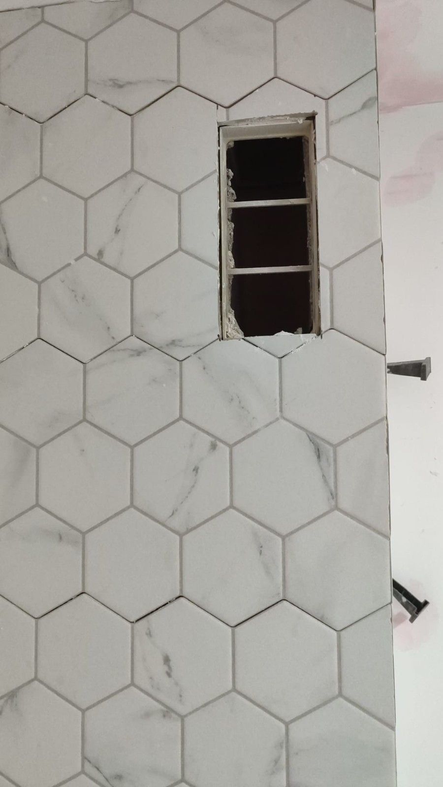 Pared con azulejos hexagonales blancos y una pequeña abertura rectangular para la ventana.