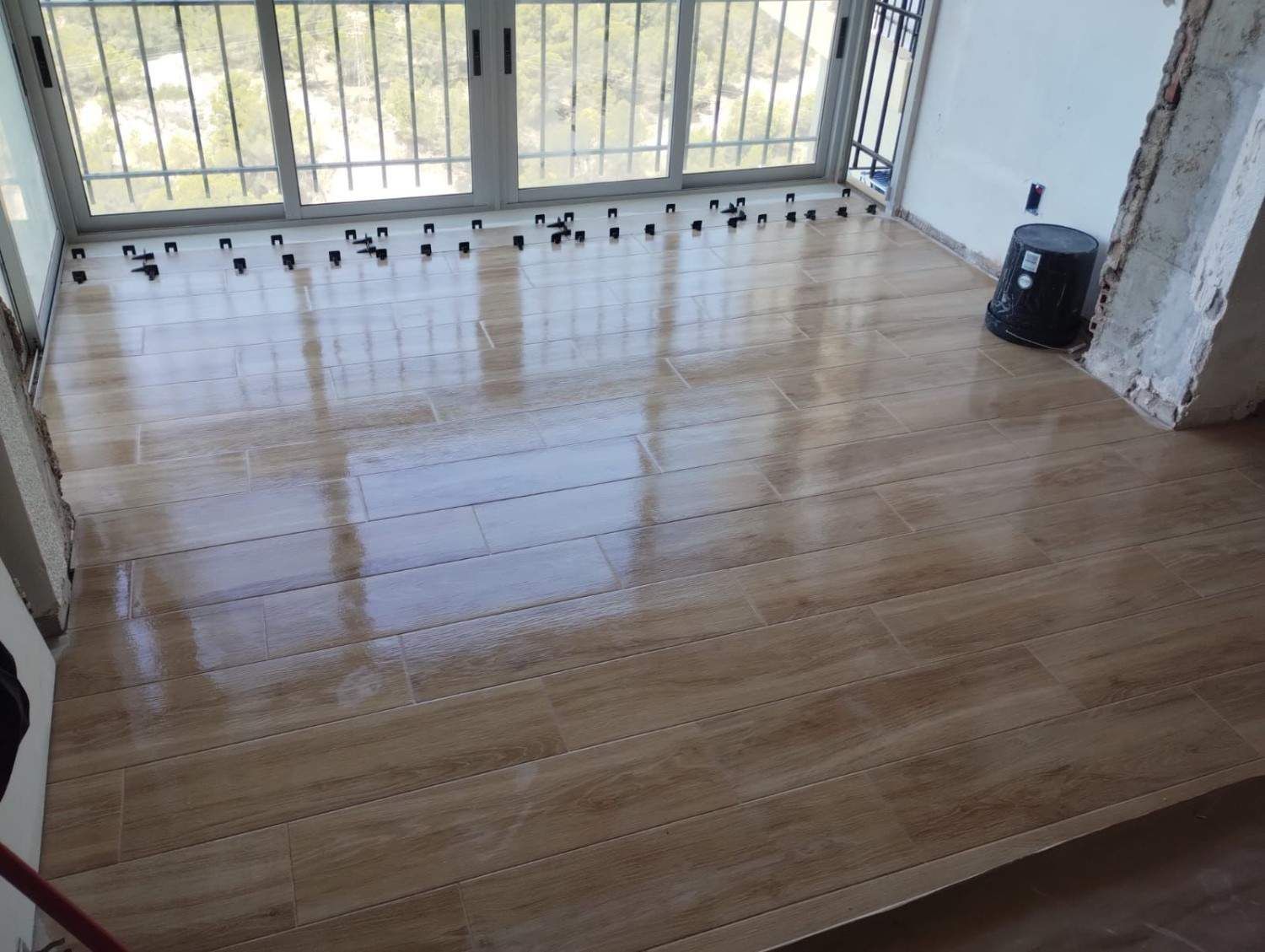 Habitación vacía con suelo de madera reluciente y grandes ventanales que dan a un balcón.