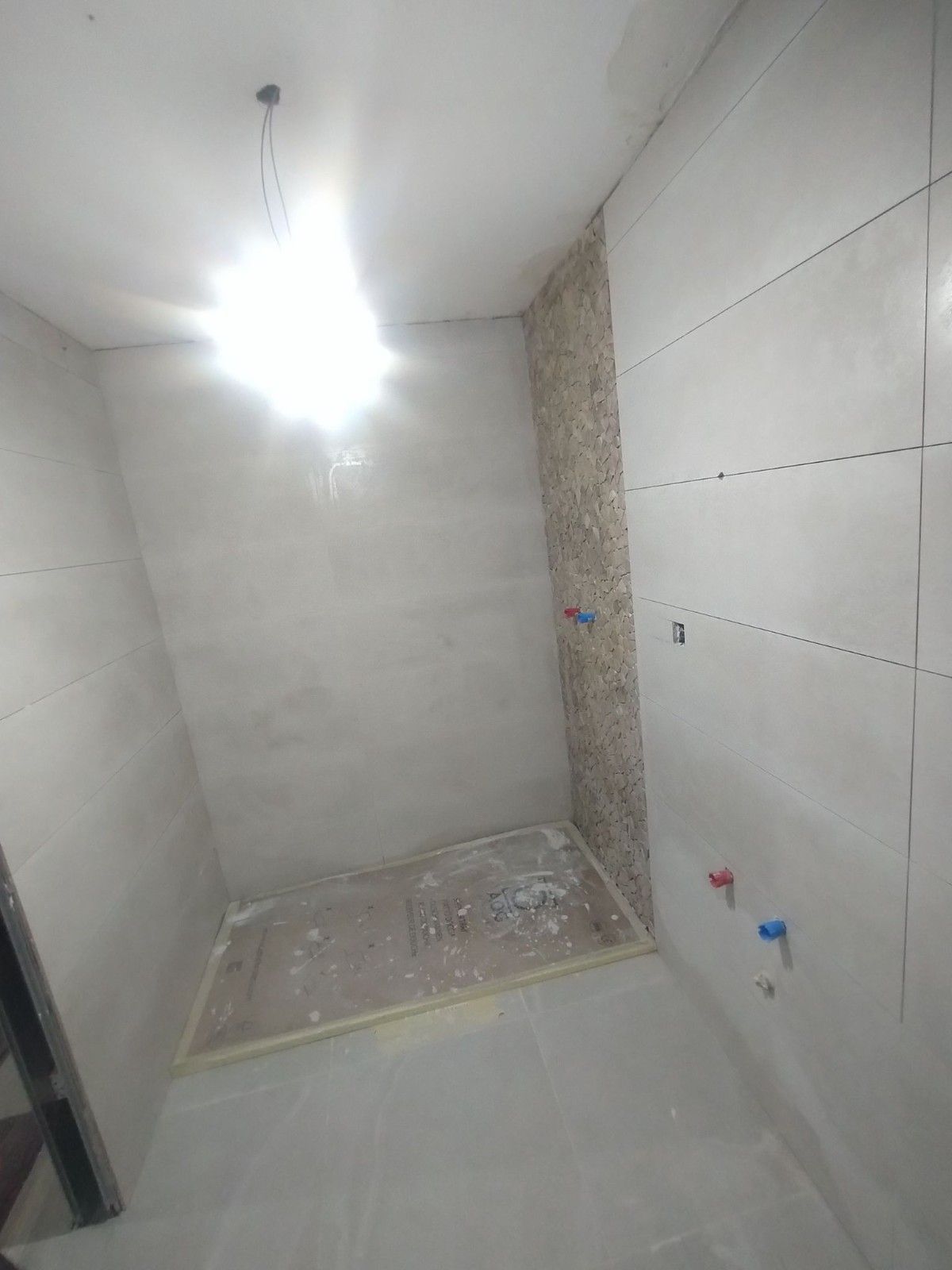 Cabina de ducha vacía en construcción con paredes blancas y desagüe en el suelo.