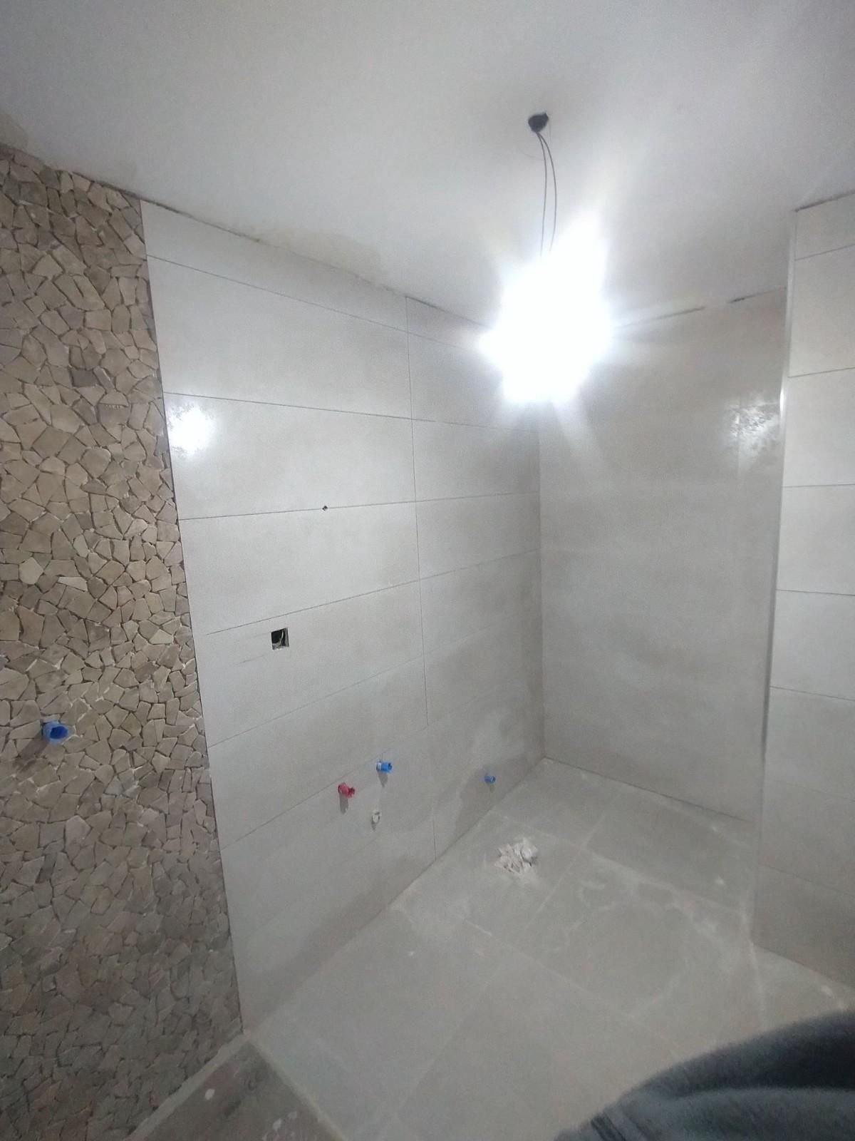 Baño vacío en construcción, con azulejos, cableado a la vista y una luz de techo brillante.