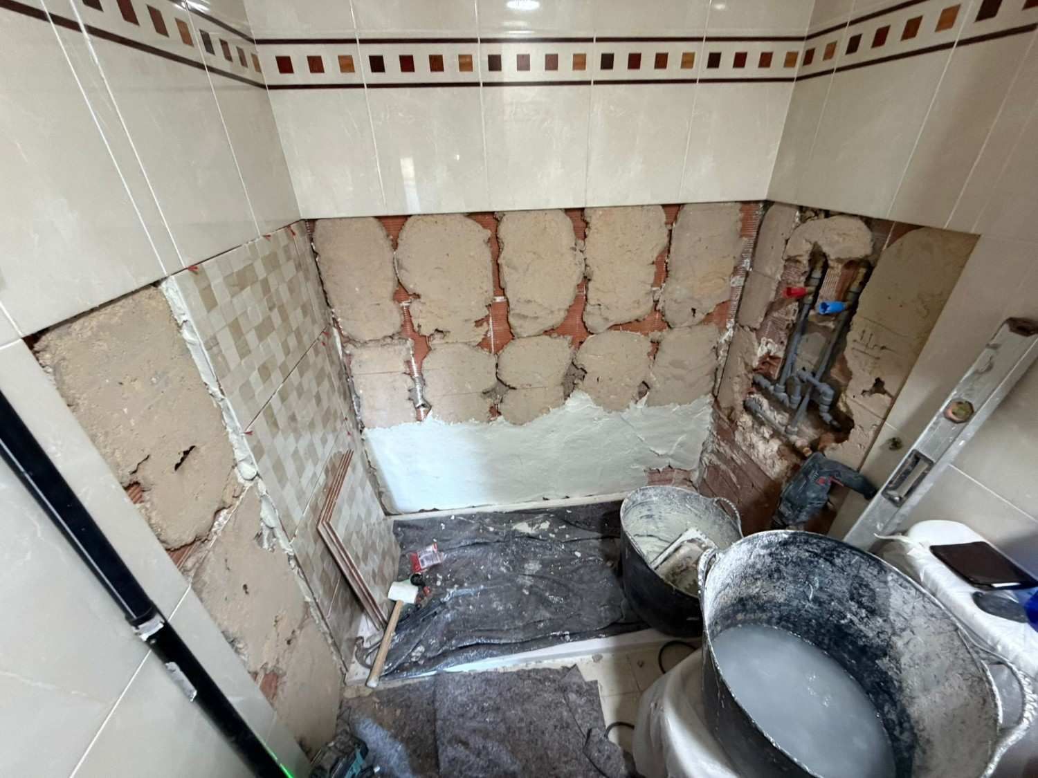 Baño parcialmente reformado con paredes al descubierto, escombros en el suelo y una escalera a la derecha.