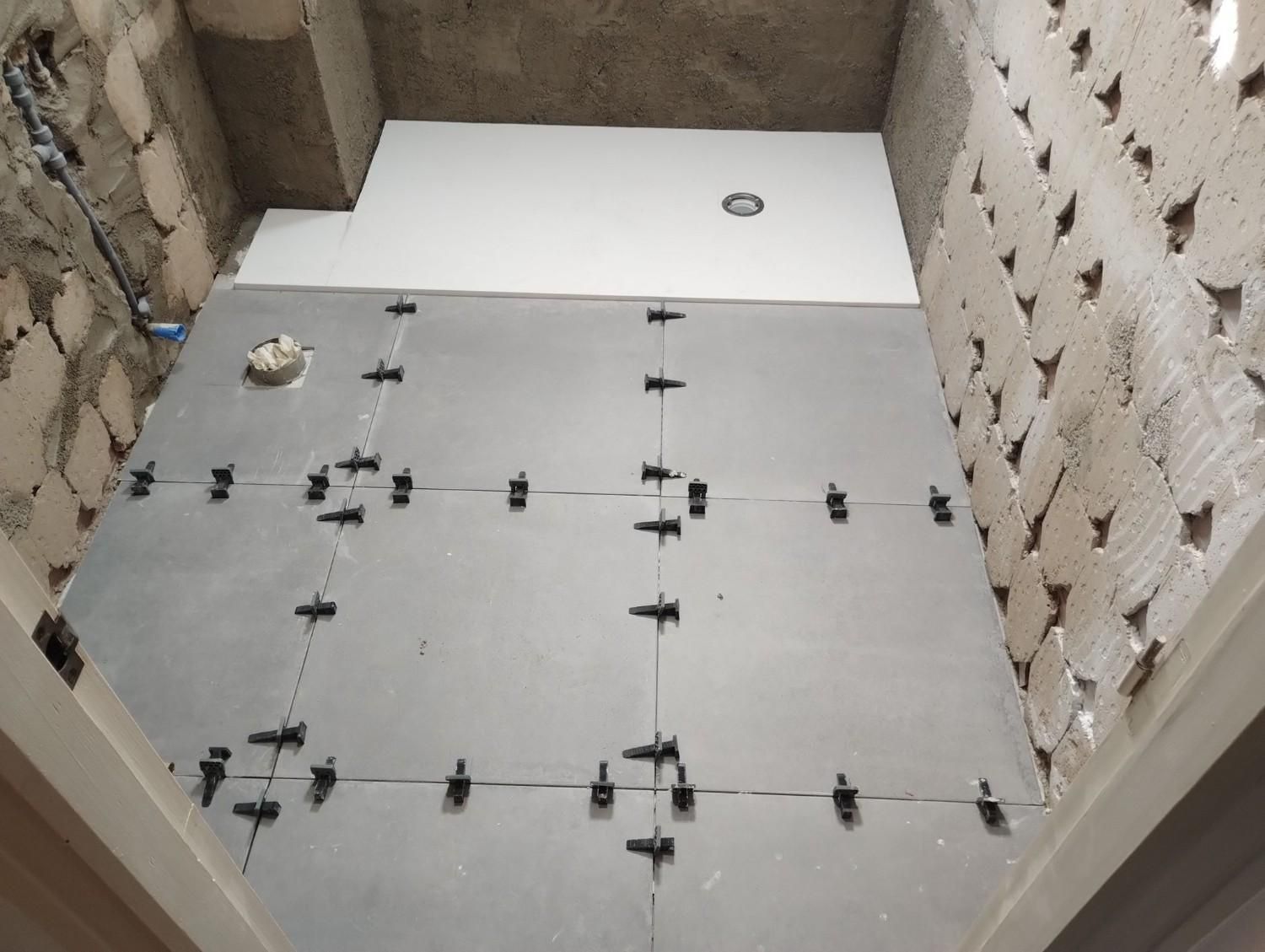 Suelo del baño parcialmente alicatado con paneles grises, separadores negros y una sección blanca en la parte trasera.