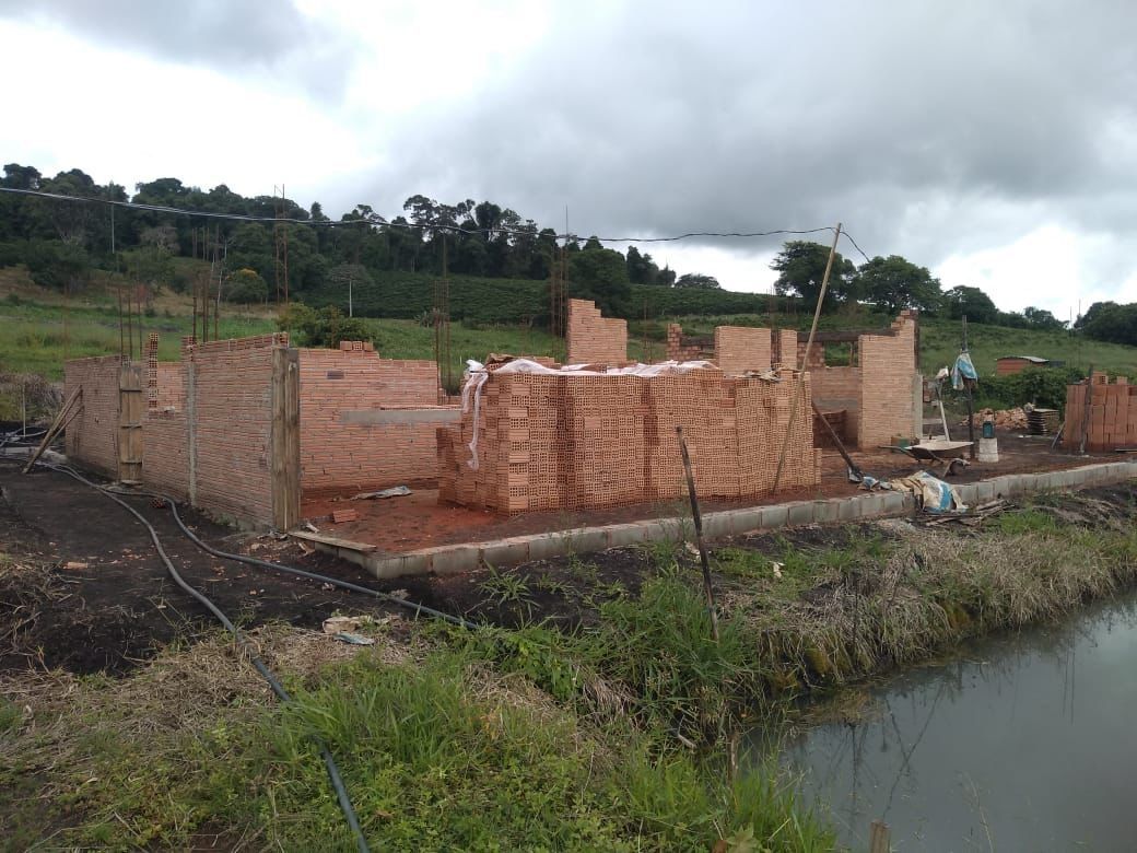 Casa de ladrillo parcialmente construida junto a un canal fangoso bajo un cielo nublado.