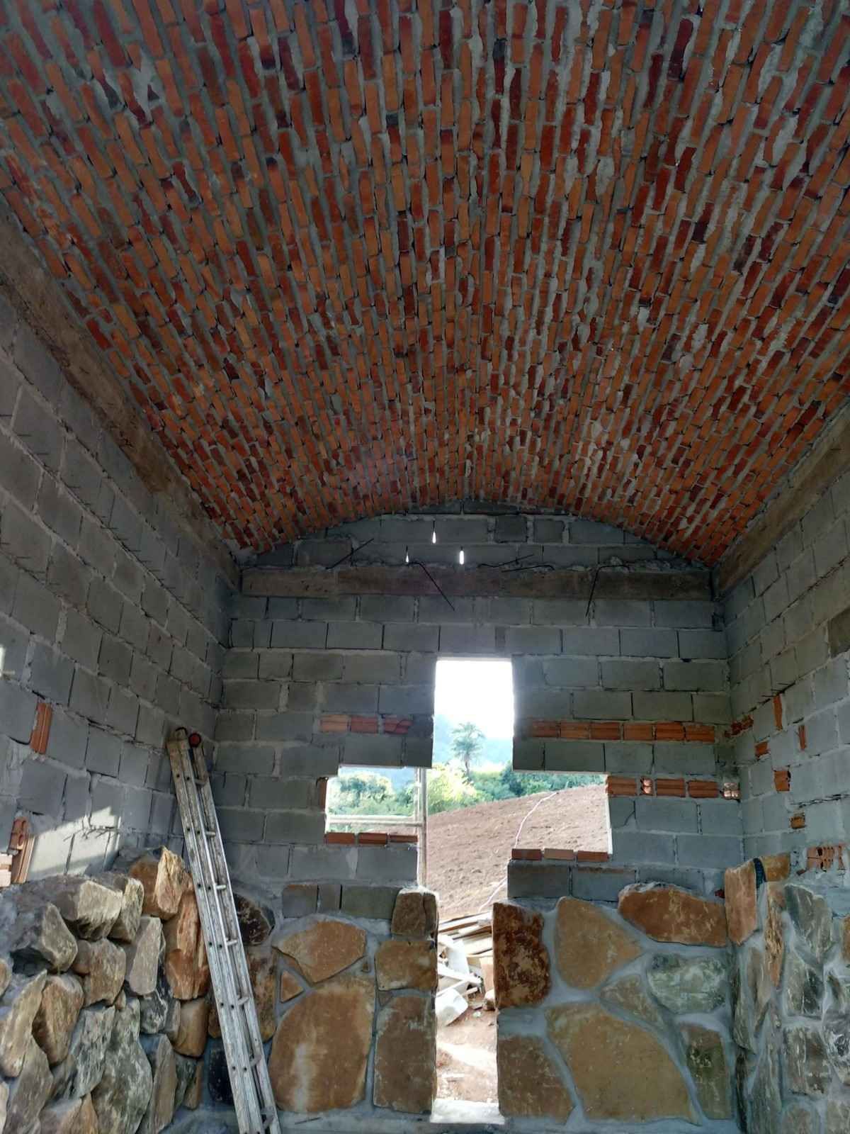 Habitación de piedra en construcción con techo abovedado de ladrillo y puerta abierta al exterior.