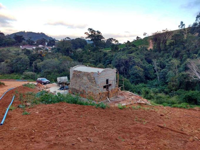 Ladera rural con una pequeña estructura de hormigón, tierra roja en primer plano y densos árboles verdes al fondo.