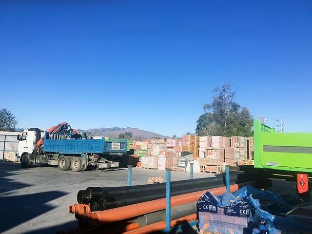 Un camión azul está estacionado en un estacionamiento al lado de un contenedor de basura verde.