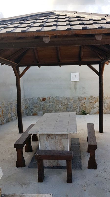Un cenador de madera con una mesa y bancos debajo.