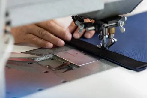 Eine Hand näht mit der Nähmaschine blauen Stoff, während eine Hand das Material führt.