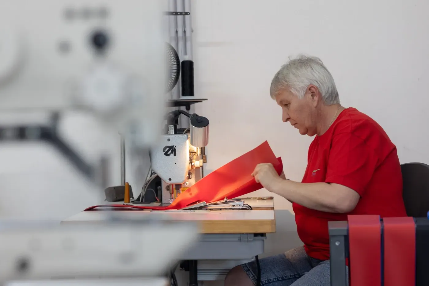 Eine Person in einem roten Hemd näht roten Stoff an einem Arbeitstisch in einer Werkstatt