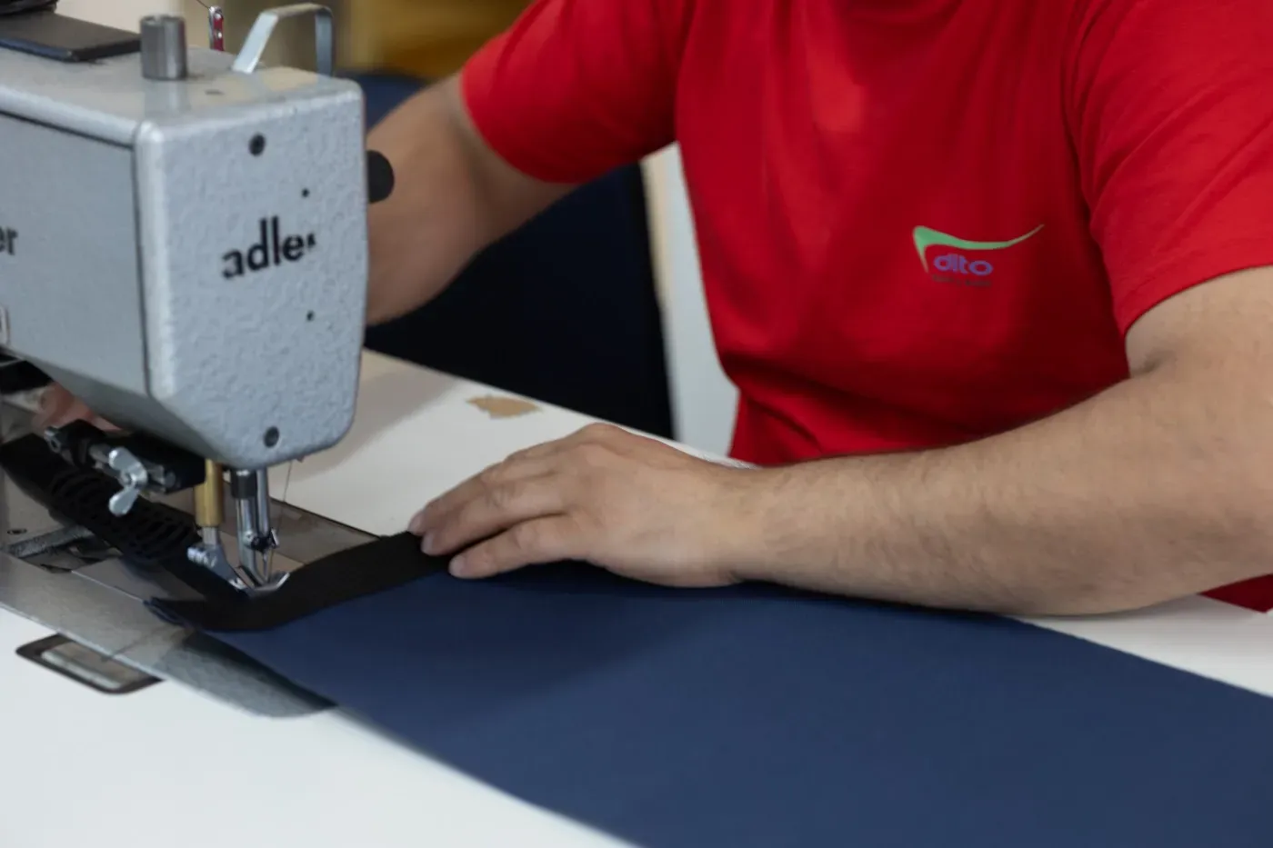 Person, die an einem Arbeitstisch dunkle Stoffe an einer Industrienähmaschine näht
