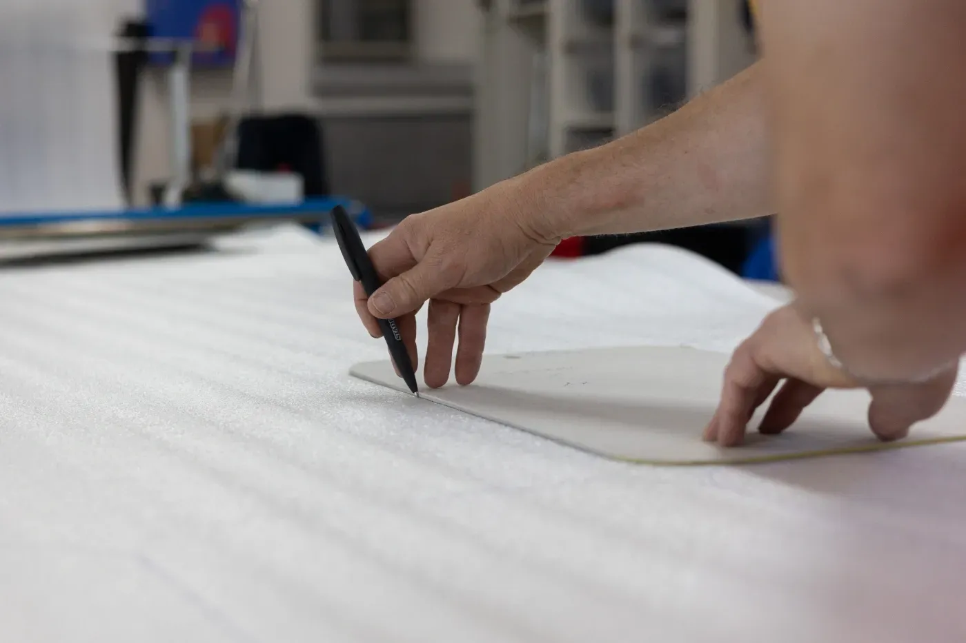 Hände markieren weißen Stoff mit einem Bleistift in einer Werkstattumgebung