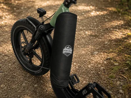 Schwarzes Elektrofahrrad mit einer Tragetasche am Frontrahmen, das auf einem Schotterweg im Freien abgestellt ist.