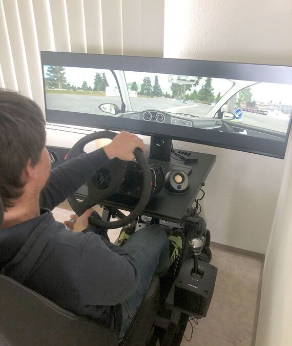 Person seated at a racing simulator steering wheel with a wide monitor showing a driving game.