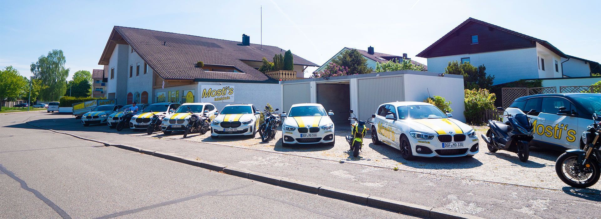 Polizeiwagen parken vor einem Gebäude in einer sonnigen Straße, rechts daneben steht ein Motorrad.