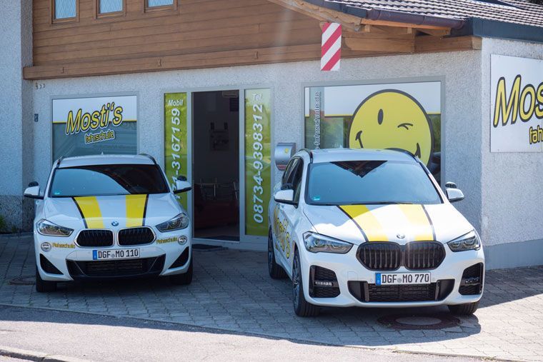 Zwei weiße Sportwagen mit gelben Rennstreifen parken vor einem Geschäft mit einem Schild mit einem Smiley-Gesicht.