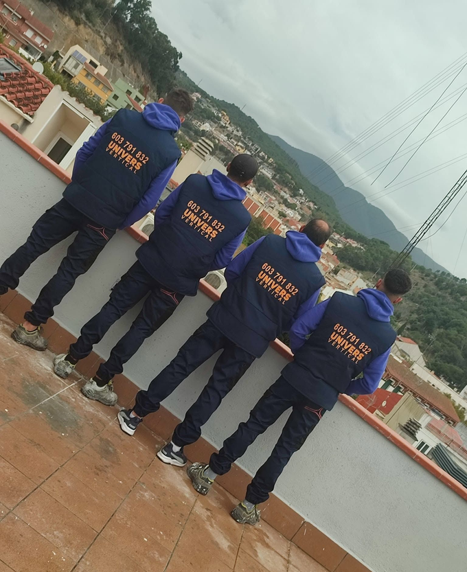 Cuatro personas con sudaderas azules están de pie en una azotea, contemplando una vista nublada de la montaña.