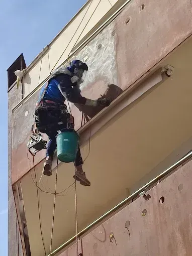 Un trabajador que trabaja mediante acceso por cuerda pinta la pared exterior de un edificio