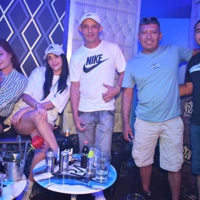 Grupo de personas en un club, sentadas y de pie, alrededor de una mesa con bebidas.