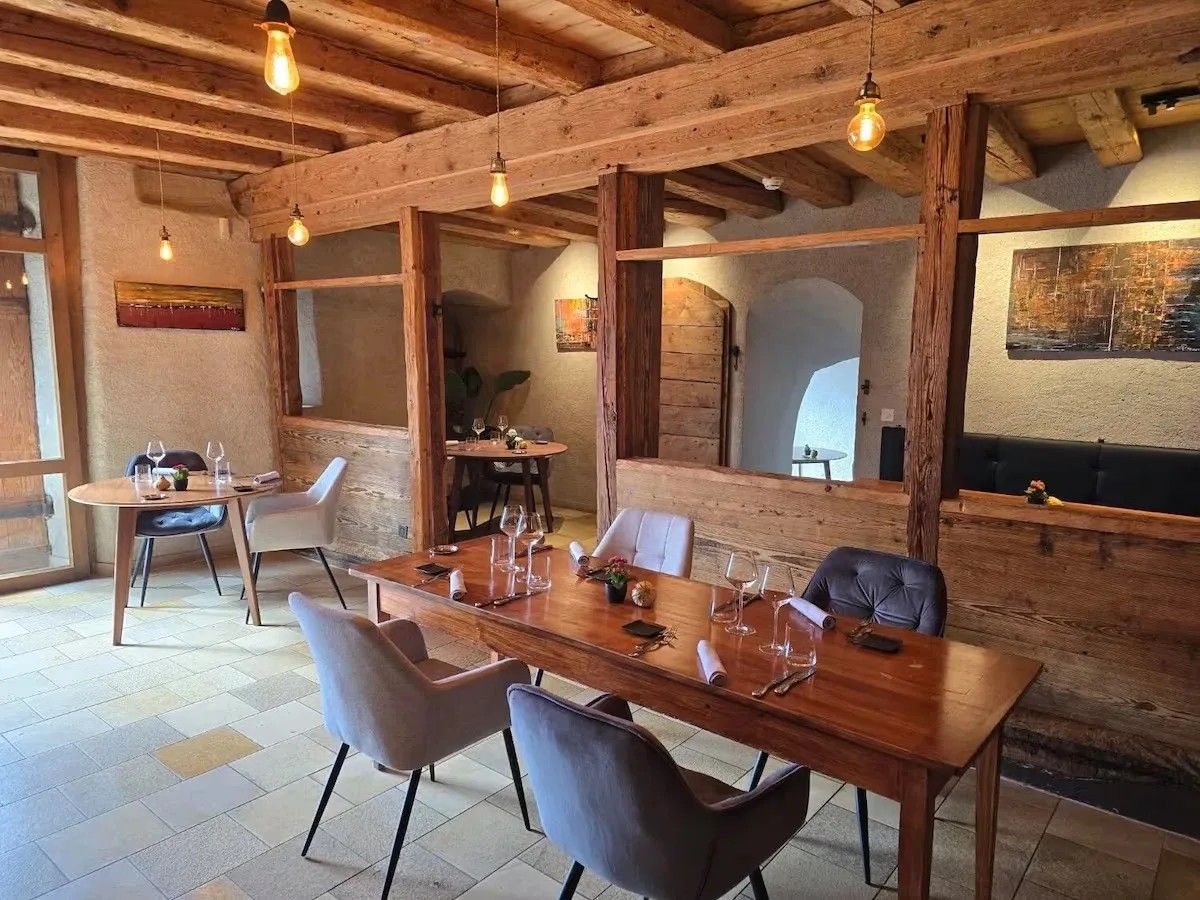 Salle à manger aux poutres et cloisons de bois ancien, tables en chêne et fauteuils gris