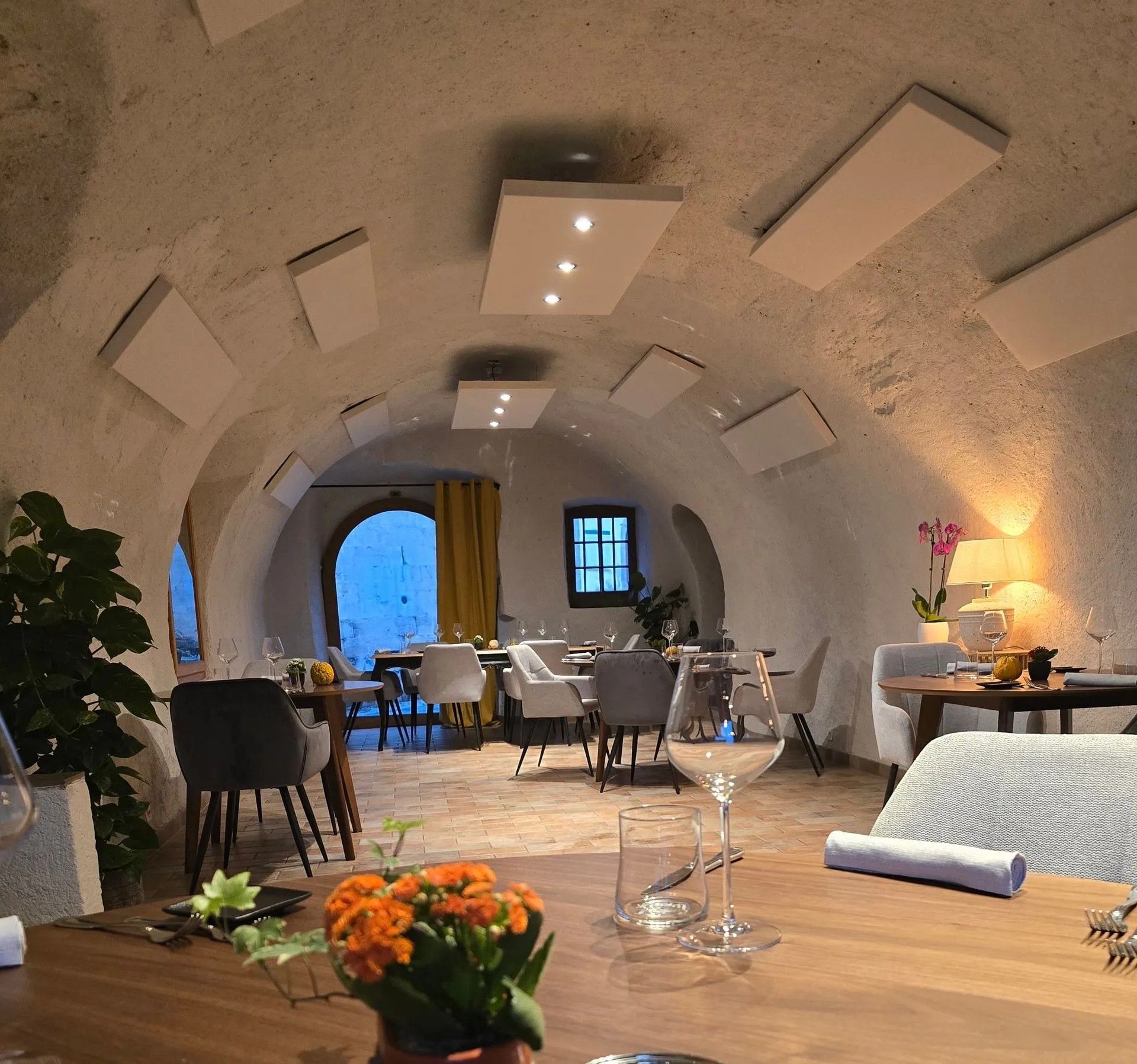 Salle voûtée en pierre blanche, tables dressées et fleurs fraîches