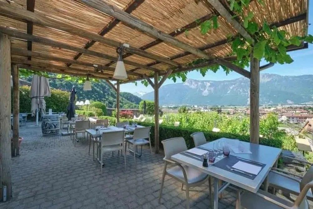 La terrasse sous sa pergola, tables dressées face aux montagnes du Chablais