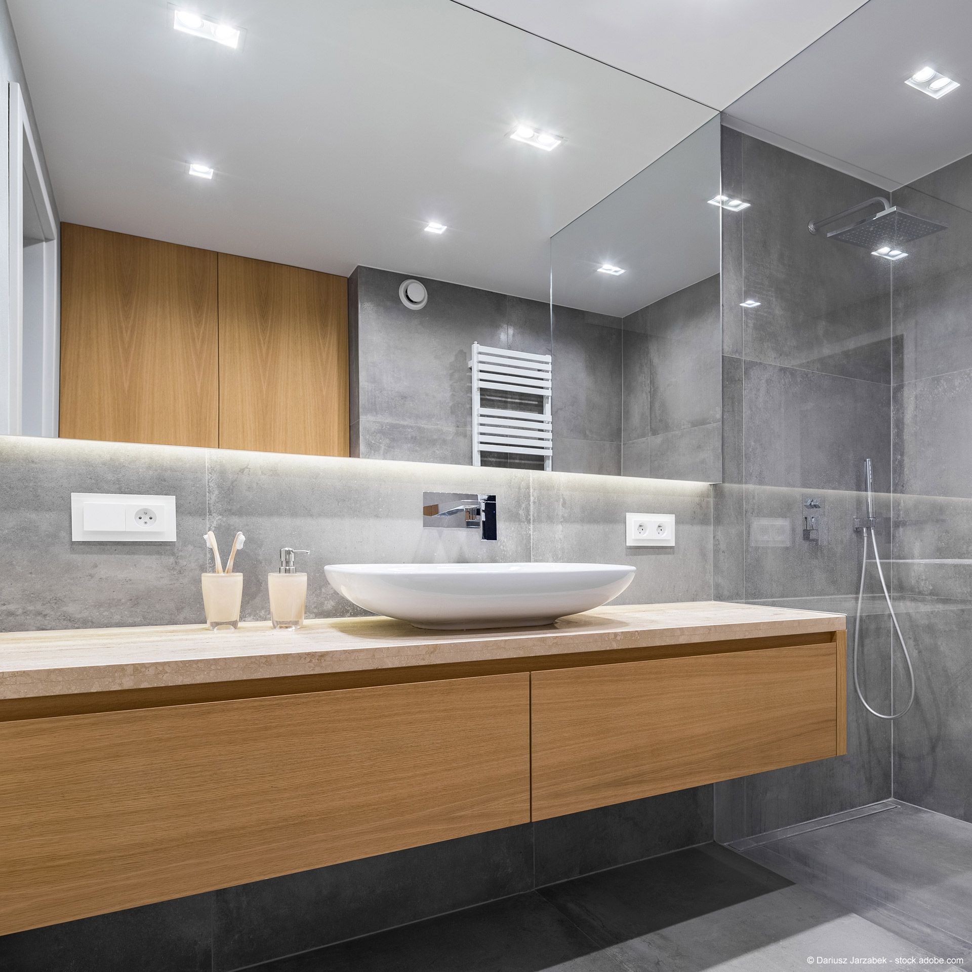 Modernes Bad mit großem Wandspiegel, Holz-Waschtisch und Dusche vor grauen Fliesen.