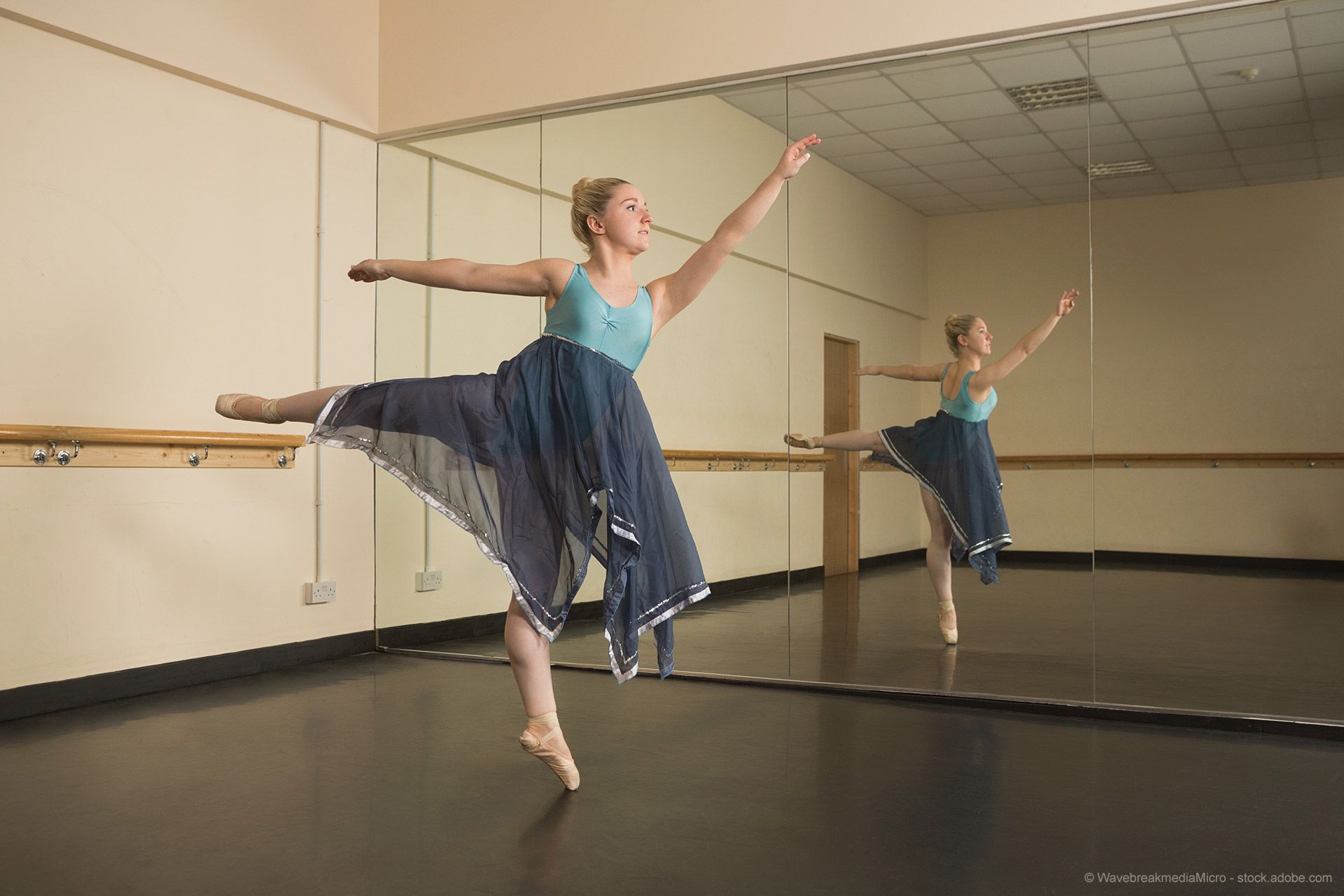 Ballerina im blauen Kleid spiegelt sich verzerrungsfrei im großen Studio-Wandspiegel.