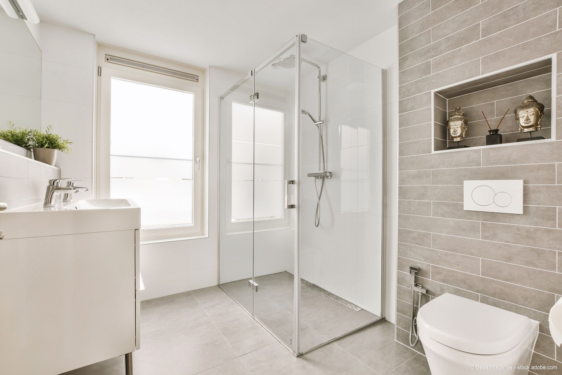 Modernes Badezimmer mit Glasdusche, weißer Toilette, Waschtisch und grau gefliesten Wänden.