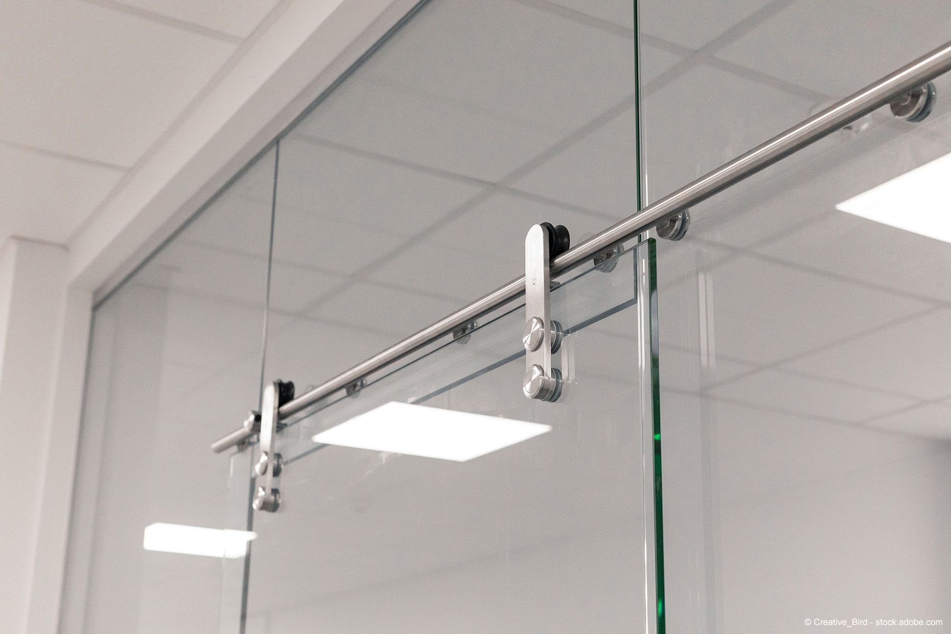 Glasschiebetür mit Edelstahlbeschlägen, eingebaut in einen weißen Büroraum.