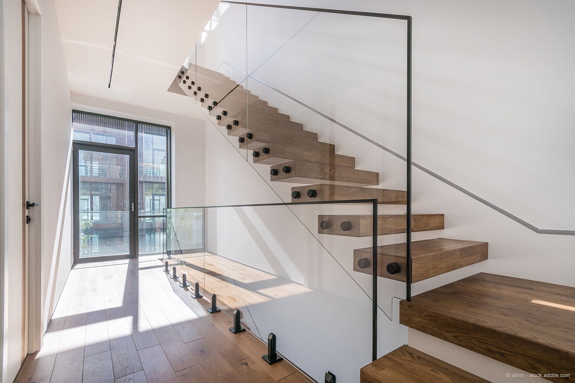 Freitragende Holztreppe mit Glasgeländer in einem hellen, modernen Haus.