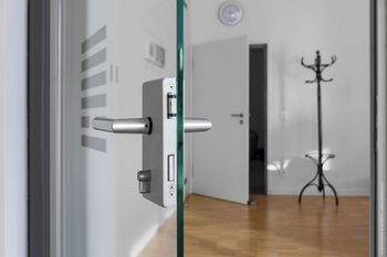 Glastür mit silbernem Griff, dahinter befindet sich ein weißer Innenraum mit Garderobe.